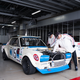 a white and blue 1972 gt-r in a garage, being worked on by two older men in clothing from the car's period